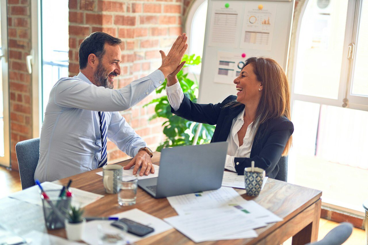 Colleagues laughing and high-fiving in a bright meeting